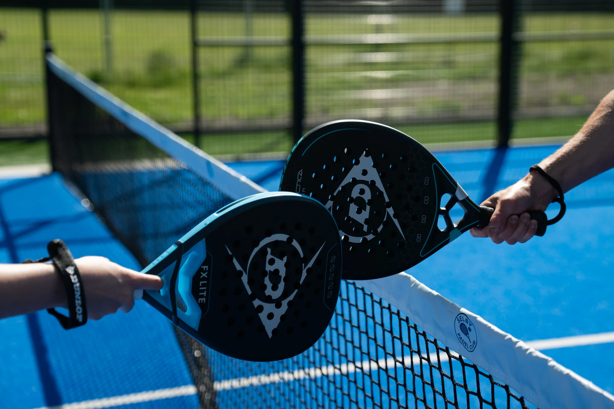 Two players touching padel rackets across the net on a blue court