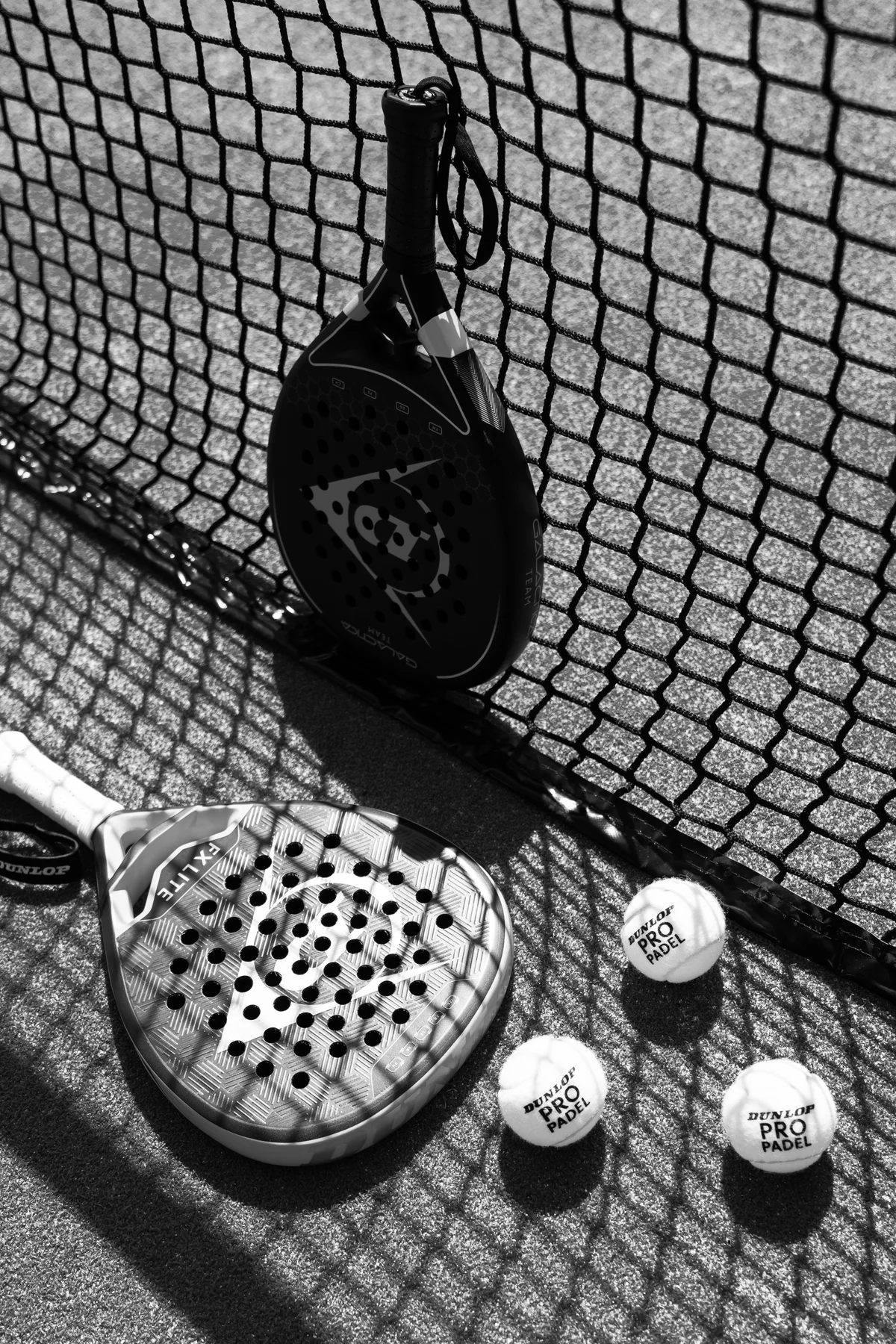 Black-and-white photograph of two padel rackets and balls beside the net