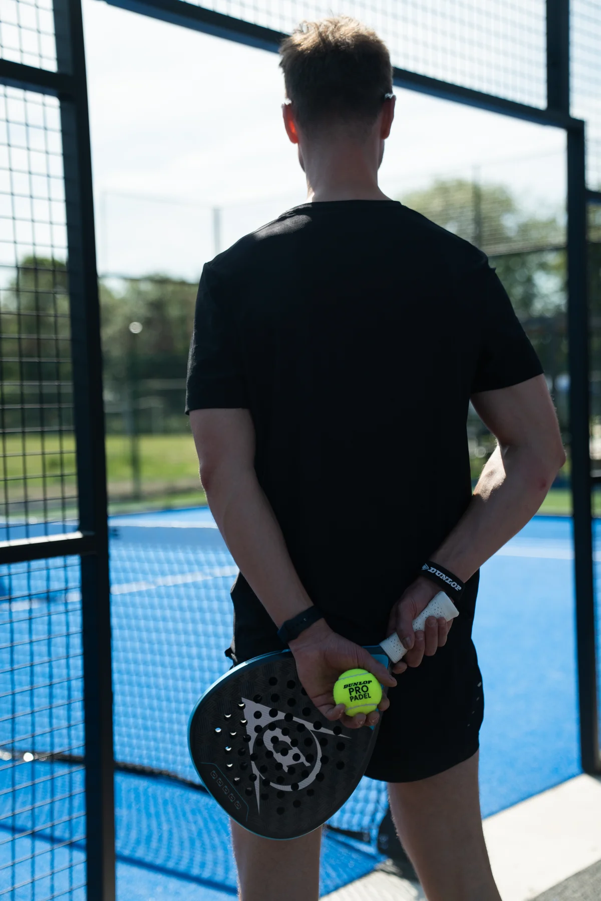A player holding a racket and ball at the entrance to a blue padel court