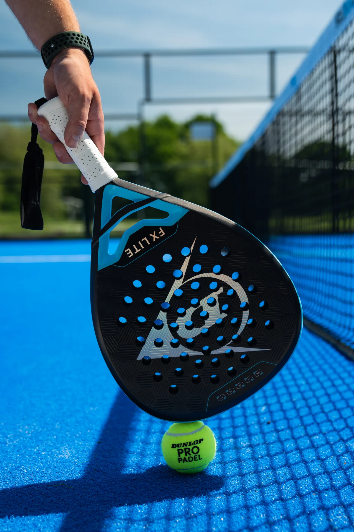 A player holding a padel racket just above a yellow ball on the blue court